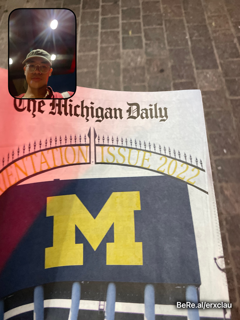 Eric Lau wearing a green hat and holding The Michigan Daily's 2022 Orientation Guide.